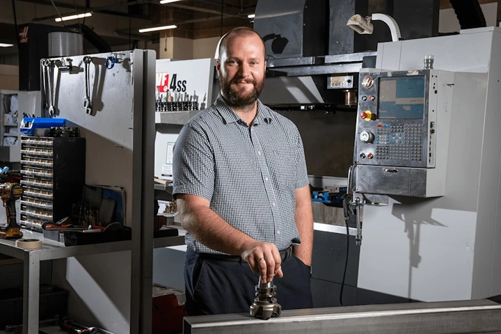 Machine Shop Manager standing proudly in front of one of his CNC Lathe Machines