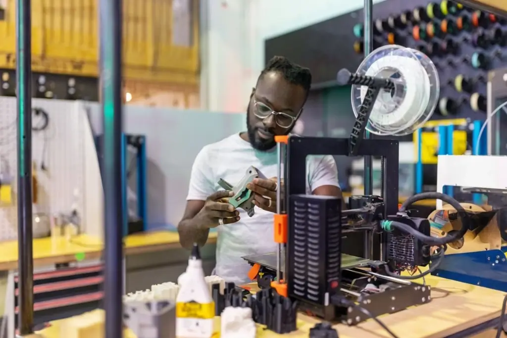 An Additive Manufacturing Technician exams a piece just made on a 3-D printer.